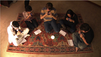 five people sit 
on a rug each playing an iPhone, Ge accompanies them on guitar